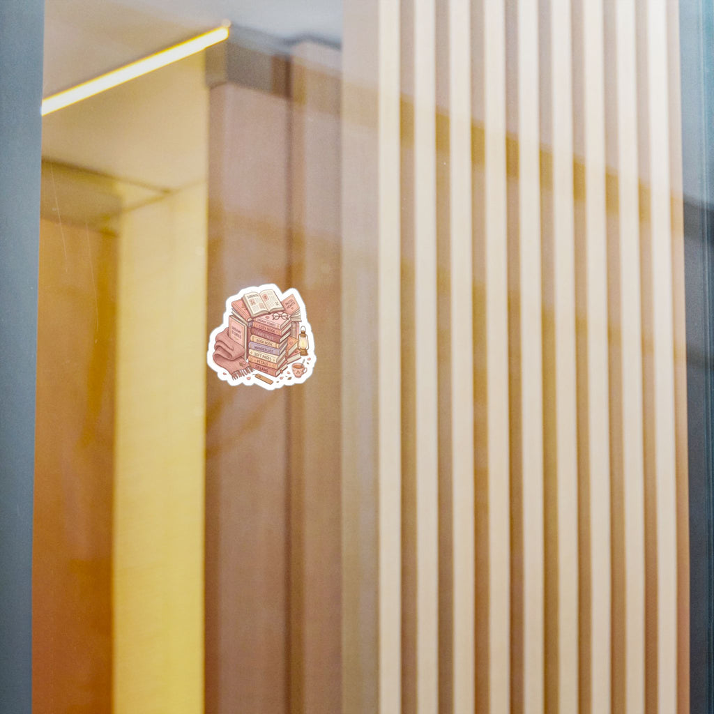 A small die-cut sticker featuring an illustrated stack of pink and beige layered cakes with a white border, shown on a reflective glass surface with warm-toned interior panels in the background.