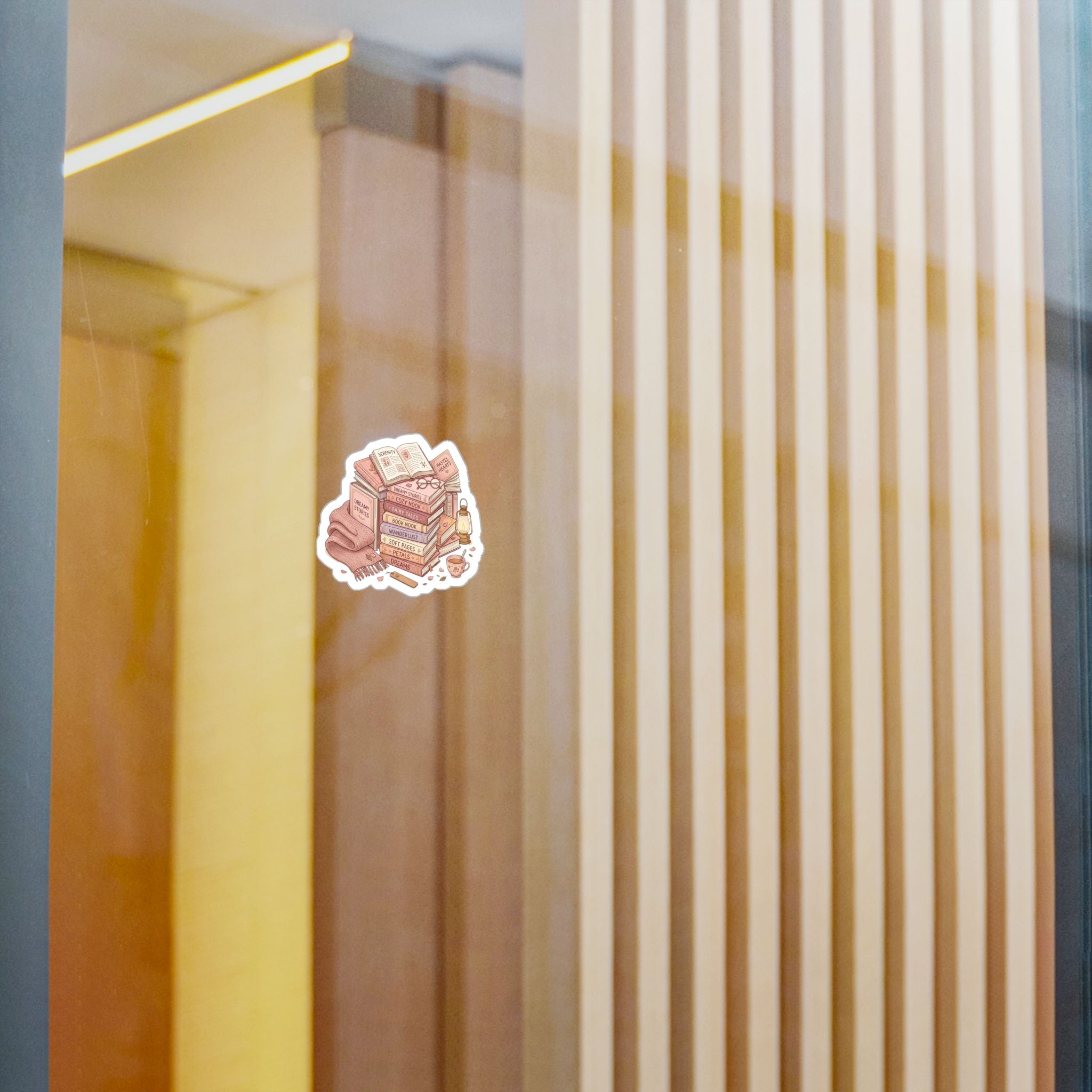 A small die-cut sticker featuring an illustrated stack of pink and beige layered cakes with a white border, shown on a reflective glass surface with warm-toned interior panels in the background.