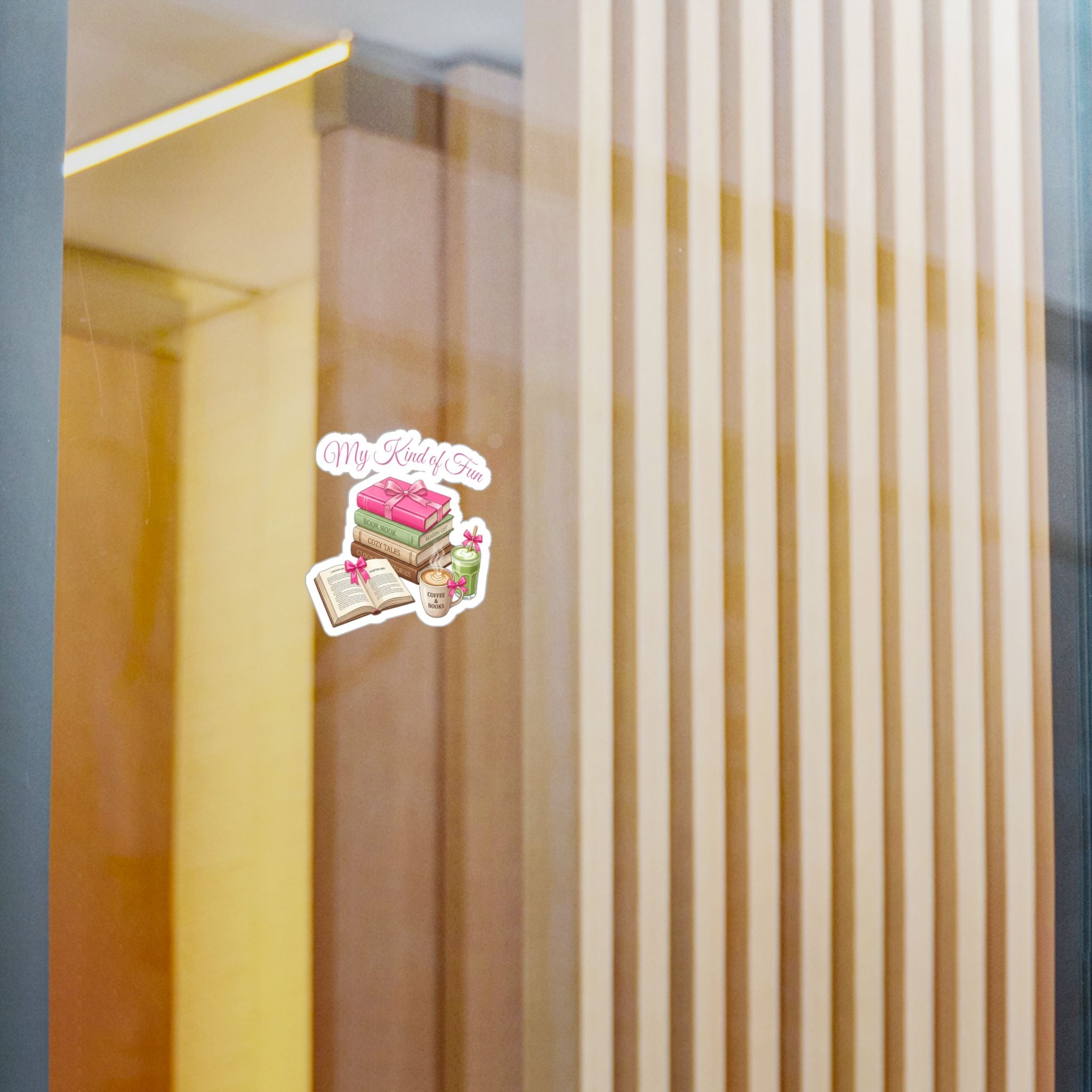 A small die-cut sticker with the text 'My Books' and an illustration of a pink frosted cake, an open book, and a small cup, shown applied to a glass door in a modern interior setting.
