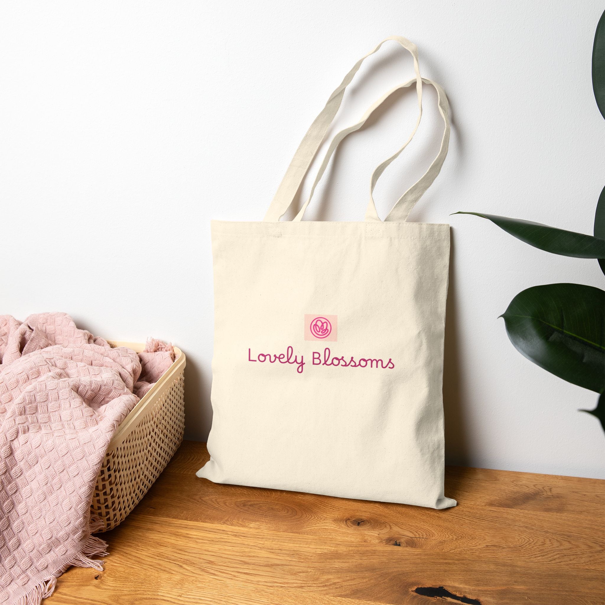 Beige tote bag with a design and text on a wooden surface with a white wall and plant in the background