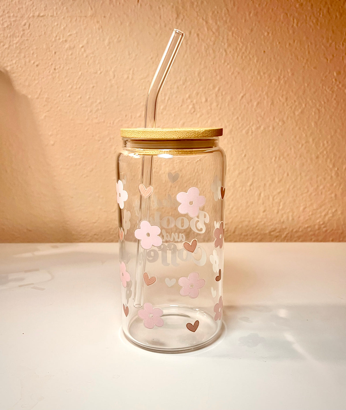 16 ounce glass drink cup with the words “fueled by Books and Coffee,” at the center of the front side cup. There are also pink cherry flowers and light brown small hearts scattered around the cup as the design. The words also contains these same color tones. Overall the cup is a very cute, girly and a great asset to have when reading a book with your favorite drink. 