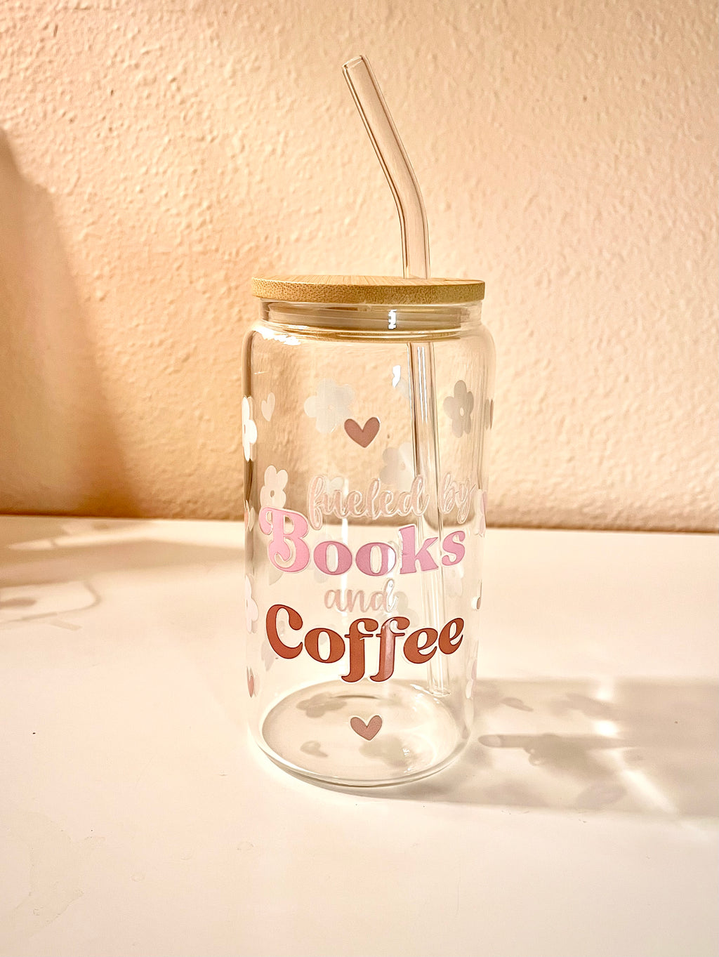 16 ounce glass drink cup with the words “fueled by Books and Coffee,” at the center of the front side cup. There are also pink cherry flowers and light brown small hearts scattered around the cup as the design. The words also contains these same color tones. Overall the cup is a very cute, girly and a great asset to have when reading a book with your favorite drink. 