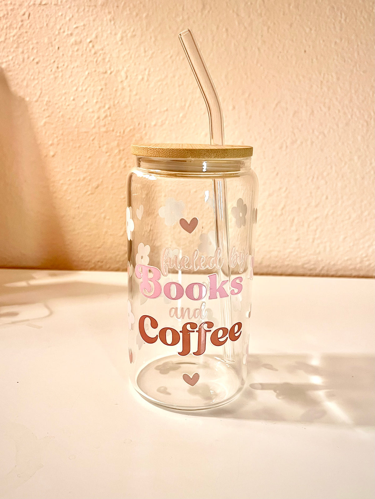 16 ounce glass drink cup with the words “fueled by Books and Coffee,” at the center of the front side cup. There are also pink cherry flowers and light brown small hearts scattered around the cup as the design. The words also contains these same color tones. Overall the cup is a very cute, girly and a great asset to have when reading a book with your favorite drink. 