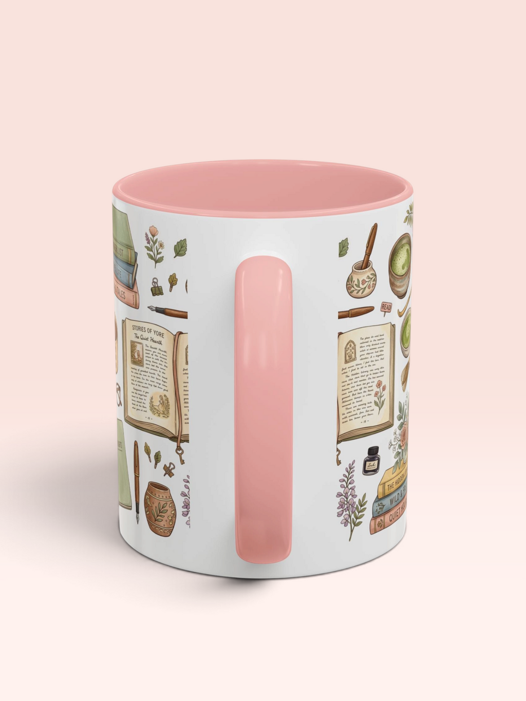 A white ceramic mug with a pink interior and handle, decorated with vintage-style botanical illustrations and book pages, shown on a soft peach-pink background.