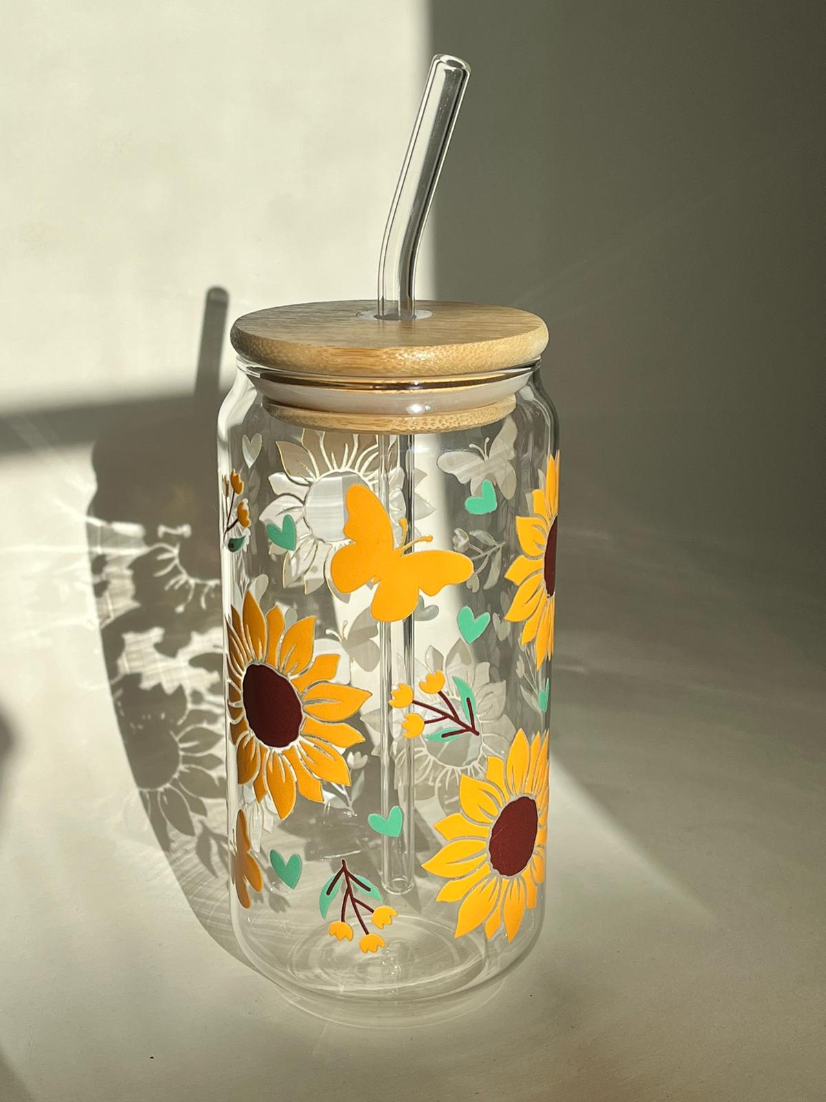A borosilicate glass cup with a wooden bamboo lid and a glass straw, decorated with a sunflower and hearts pattern.
