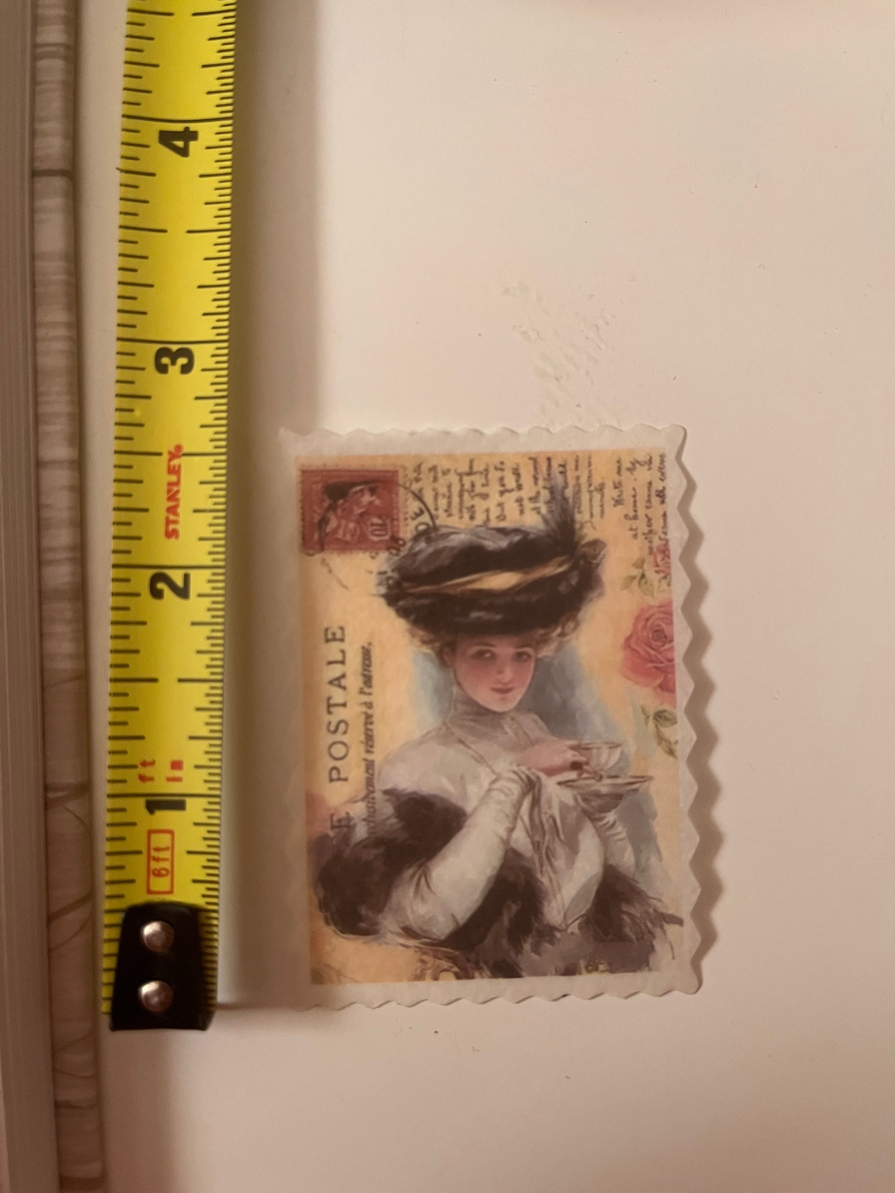 A vintage-style postage stamp featuring an illustration of a woman in a hat, shown next to a yellow Stanley tape measure on a light beige surface.